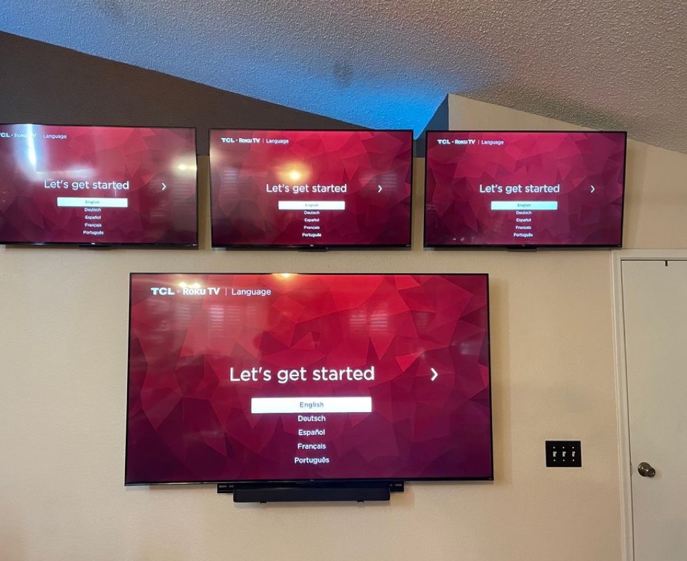 Four TVs mounted on one living room wall with a soundbar